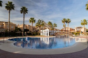 A swimming pool with a bridge, palm trees, and buildings in the background. - Private Chill-out | NETFLIX| 8min Beach | Family (Vera)