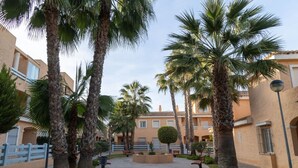 Un patio con palmeras, una fuente central y un edificio con tejado de azulejos.