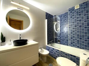 A modern bathroom with a black sink, a round mirror, a bidet, and a bathtub with blue mosaic tiles. - Private Chill-out | NETFLIX| 8min Beach | Family (Vera)
