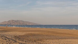 Una playa con una montaña al fondo y una persona caminando sobre la arena.