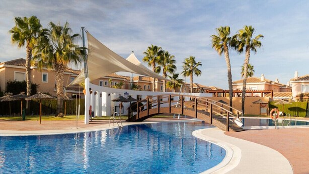 Piscina con un puente, palmeras y un toldo blanco.