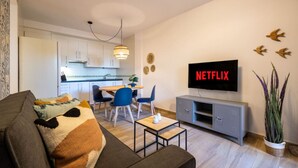 Una sala de estar moderna con un sofá, un televisor montado en la pared y una zona de comedor al fondo.