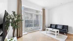A modern living room with a large sliding glass door, a black sofa, a white coffee table, and a TV on a stand. - Studio Near Dubai Mall Burj Khalifa (Dubai)