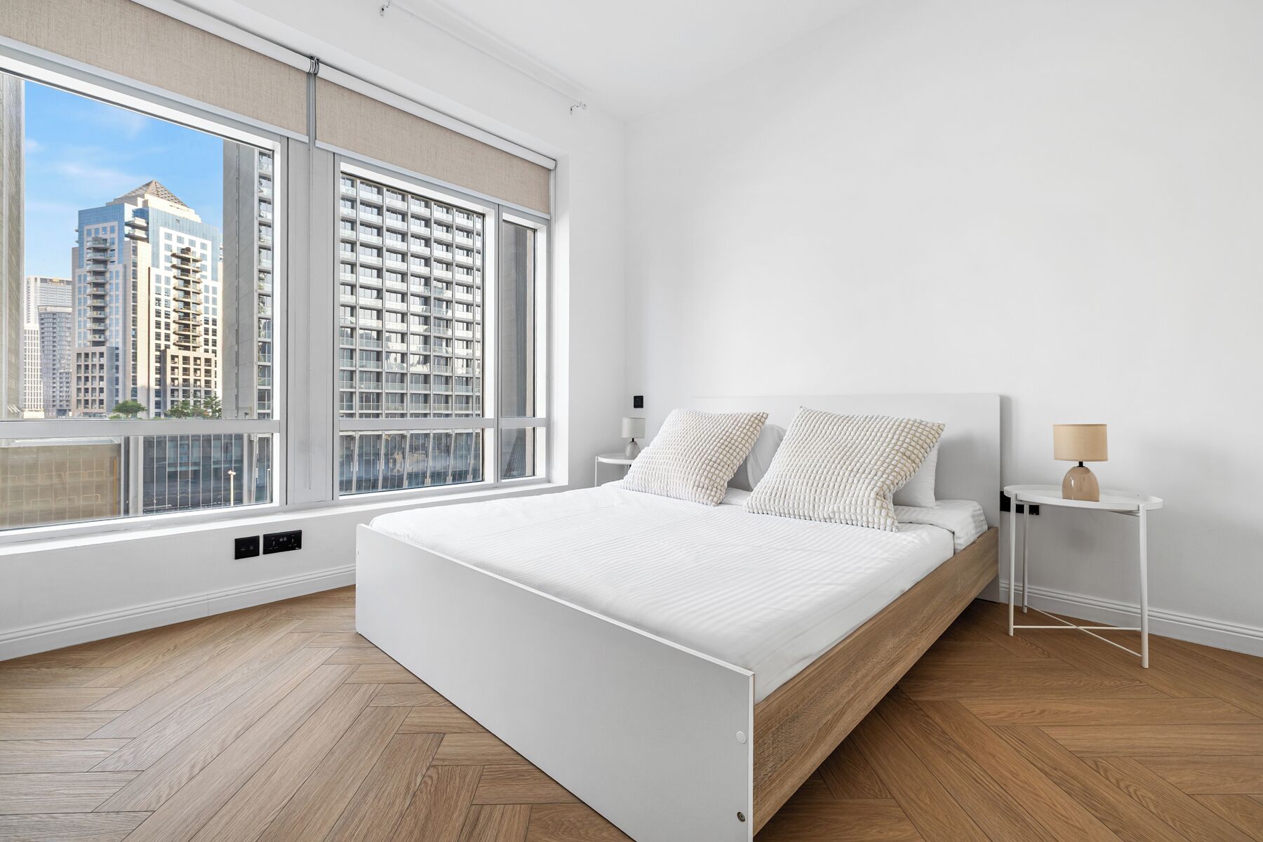 A modern bedroom with a large window, a bed, a nightstand, and a lamp.