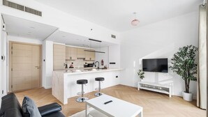 A modern living space with a sofa, a coffee table, a TV, and a kitchen area with a bar. - Studio Near Dubai Mall Burj Khalifa (Dubai)