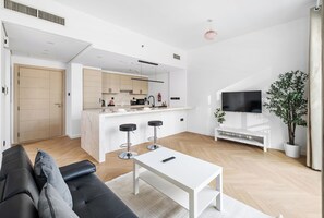 A modern living space with a sofa, a coffee table, a TV, and a kitchen area with a bar. - Studio Near Dubai Mall Burj Khalifa (Dubai)