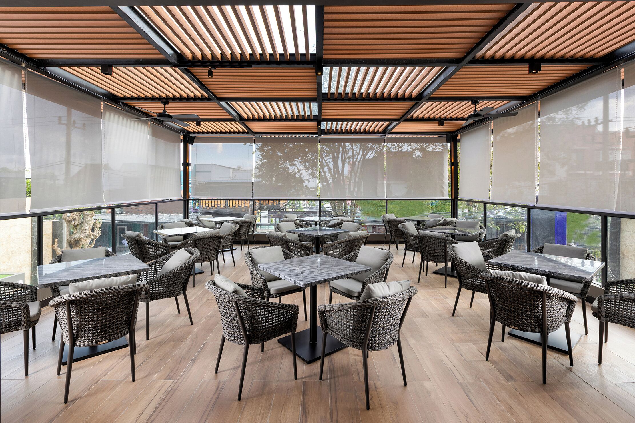 An outdoor patio with wicker furniture, glass tables, and a view of the surrounding area.