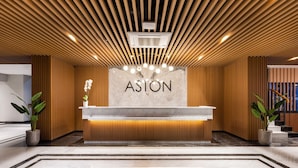 A reception desk with a wooden panel design, a marble countertop, and the word 'ASTON' on the wall. - Aston Malang Hotel & Conference Center (Malang)