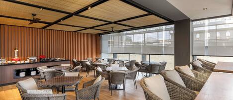 A modern restaurant with wicker furniture, a buffet area, and large windows.