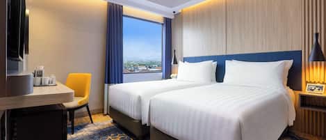 A hotel room with two beds, a desk with a TV, a chair, and a large window with a view.