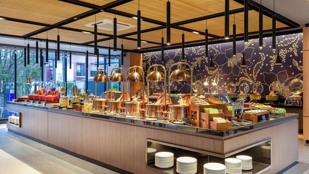 A buffet with various food items, a counter with plates, and a decorative wall with patterns. - Aston Malang Hotel & Conference Center (Malang)