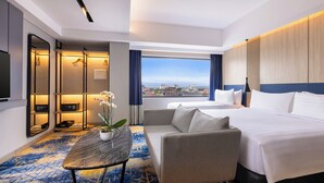 A hotel room with a bed, a sofa, a TV, a mirror, and a view of the city. - Aston Malang Hotel & Conference Center (Malang)