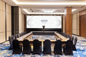 Ett konferensrum med ett långt bord, stolar och en skärm som visar texten ”ASTON MALANG HOTEL & CONFERENCE CENTER”.