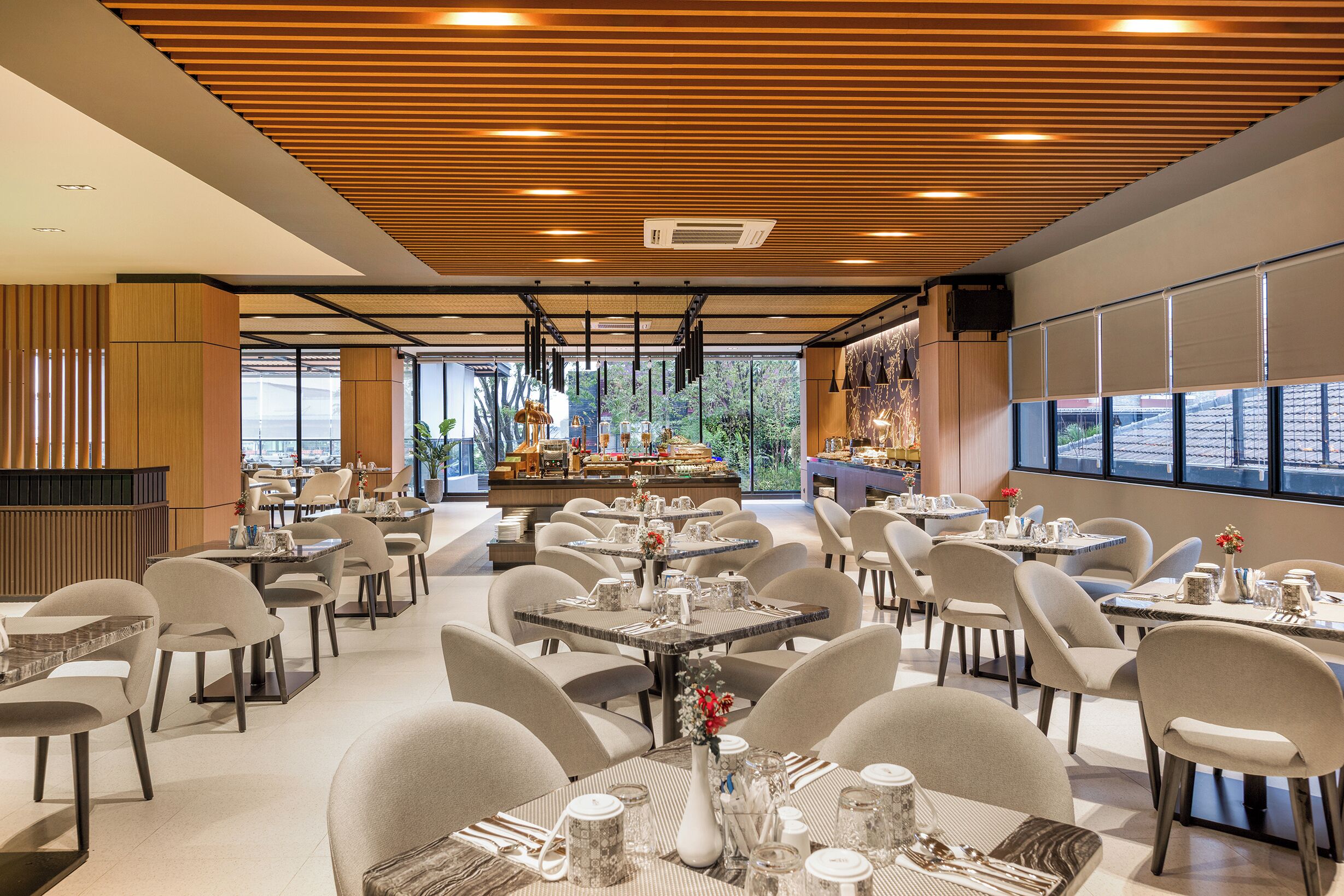 Un comedor moderno con mesas y sillas, un bufé de fondo y ventanas amplias.