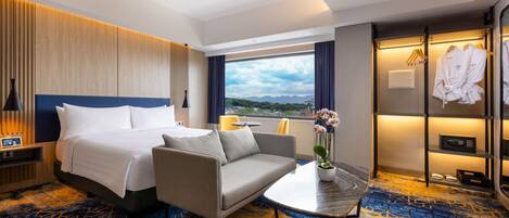A hotel room with a bed, sofa, small table, and a view of the outdoors.