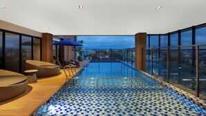 A modern indoor pool with a checkered floor, wooden seating, and large windows offering a city view. - Aston Malang Hotel & Conference Center (Malang)