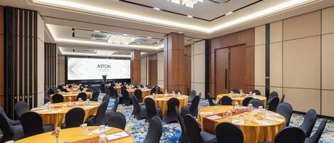 A conference room with multiple tables, chairs, and a projector screen.