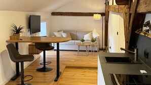 Moderni keittiö, jossa on puulattia, ruokailutila pöytineen ja tuoleineen, sohva ja televisio.