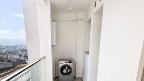 Ein Balkon mit Waschmaschine, weißen Wänden und Blick auf eine Stadtansicht.