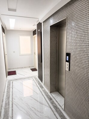 Un pasillo con pared de azulejos, suelo de mármol y un ascensor.