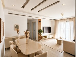 Ein modernes Wohnzimmer mit Essbereich, einem Flachbildfernseher und einem großen Fenster mit Vorhängen.