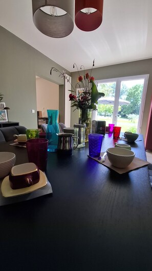 Ein Essbereich mit Tisch für zwei Personen, einer Blumenvase und einem Fenster mit Blick auf Grünflächen.