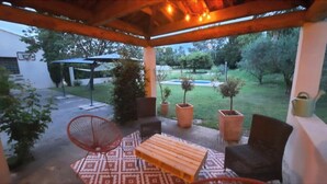Un patio couvert aménagé avec du mobilier d’extérieur, notamment une table et des chaises en bois, ainsi que des plantes en pot.