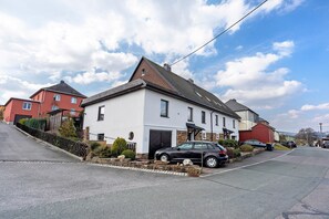 Une rue résidentielle bordée de maisons, une voiture noire garée devant l’une d’elles, et un ciel dégagé.