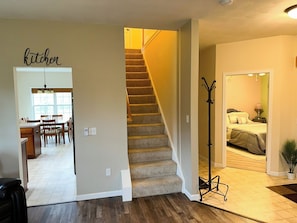 A staircase leading to a bedroom with a bed, a bedside table, and a lamp. There is a coat rack near the staircase.