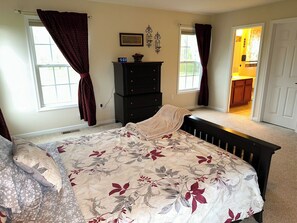 Une chambre à coucher avec un lit, une commode et deux fenêtres avec des rideaux.