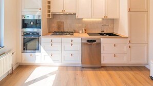 Une cuisine moderne avec des meubles blancs, des appareils électroménagers en acier inoxydable et un plancher en bois.