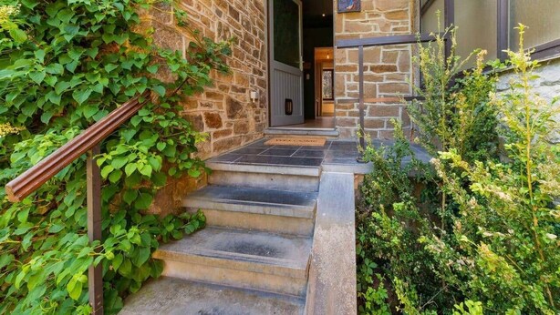 Un escalier en pierre mène à une porte sur laquelle est affiché un panneau indiquant : « Bienvenue ».