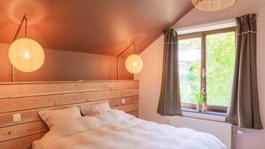 Une chambre avec une tête de lit en bois, un grand lit avec une literie blanche, deux lanternes en papier suspendues, une fenêtre avec des rideaux et un radiateur.