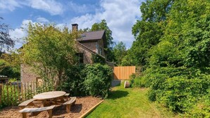 Un jardin avec une table et des bancs de pique-nique en bois, entouré d’une clôture en bois et d’une végétation luxuriante.