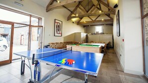 Una habitación con mesa de ping pong, mesa de billar y vigas de madera en el techo.