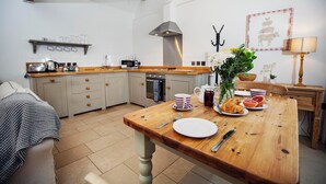 Una cocina con una mesa de madera preparada para el desayuno, una cafetera y un microondas.