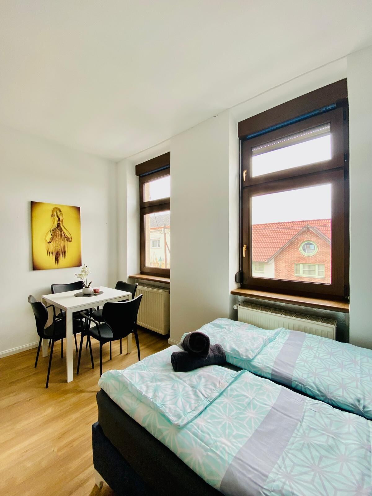 A room with a bed, a desk, and a chair. There is a window with a view of a building outside.