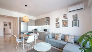Ett modernt vardagsrum med en grå soffa, ett matbord med stolar, ett litet vitt bord och en hängande lampa.