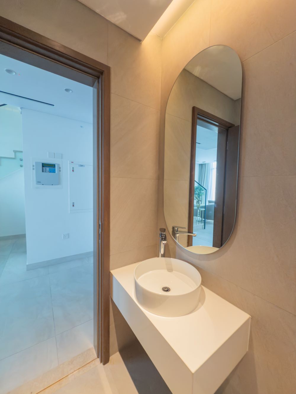 A modern bathroom with a white sink, a large mirror, and a door leading to a hallway.