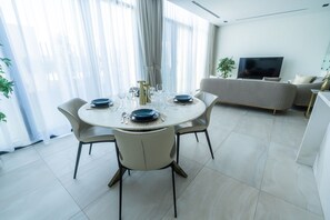 A modern dining area with a round table set for four, surrounded by chairs. A sofa and a TV are visible in the background. - Impressive townhouse in Al Danah Bay  (Ras Al Khaimah)