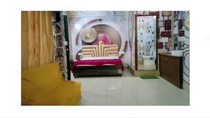 A bedroom with a bed, a yellow sofa, a wall with a decorative design, and a bathroom visible through a glass door. - MS GRAND HOTEL (Bhiwani)