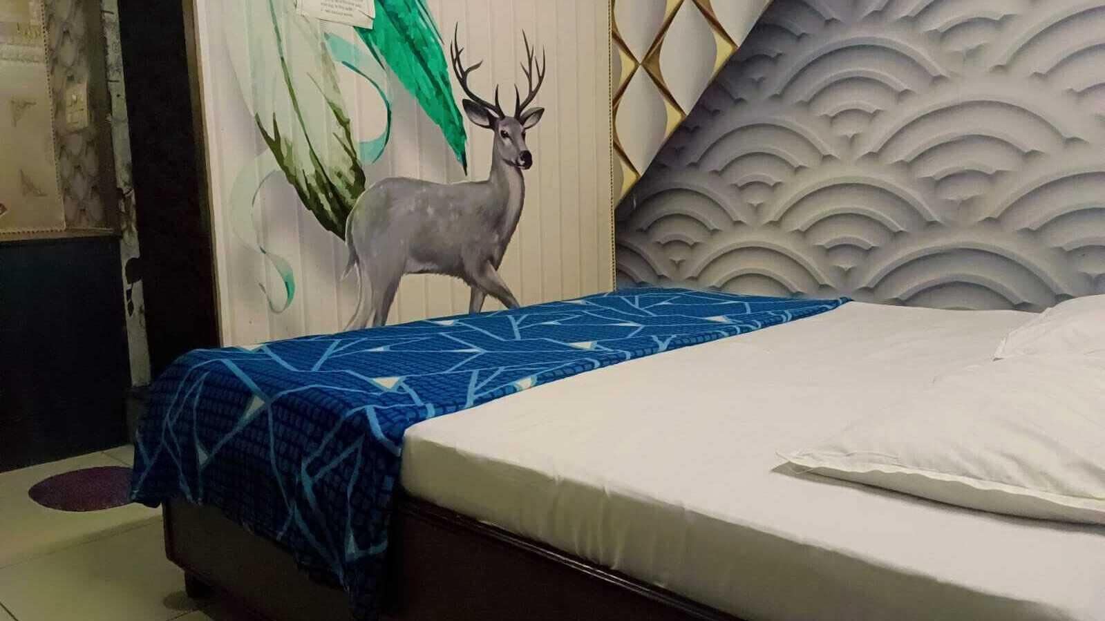 A bedroom with a bed, a blue patterned bedspread, a white pillow, and a wall mural of a deer.