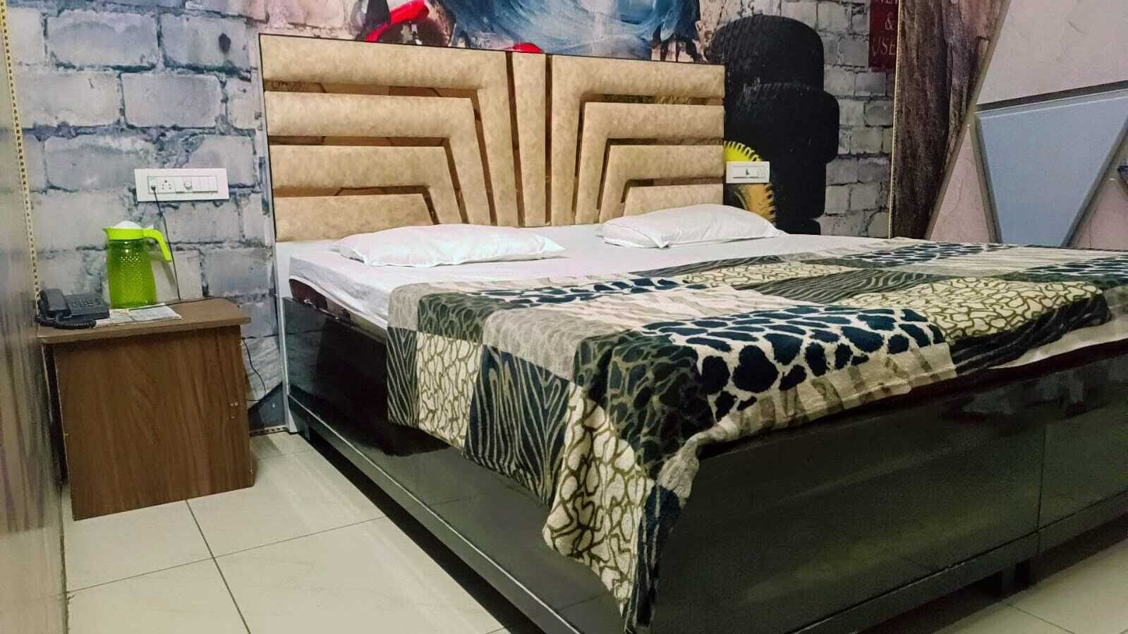 A bedroom with a bed, a wooden nightstand, a green water bottle, and a brick wall.