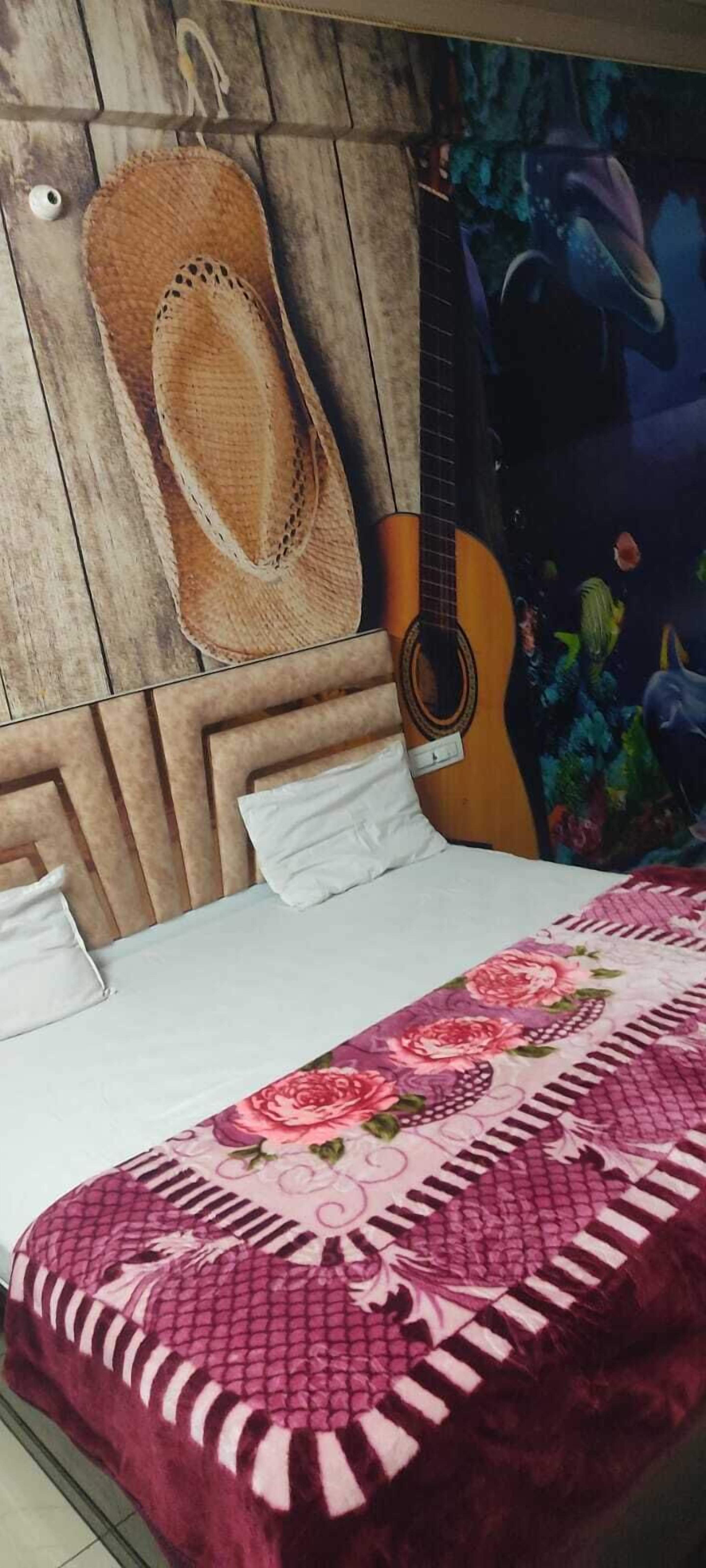 Un dormitorio con cabecera de madera, una guitarra, un tapete tejido y una colcha con motivos florales.