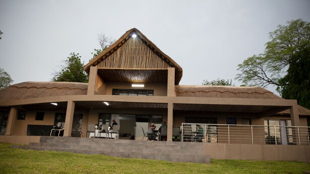 Een gebouw met rieten dak, een overdekte entree en een verhard gebied ervoor.