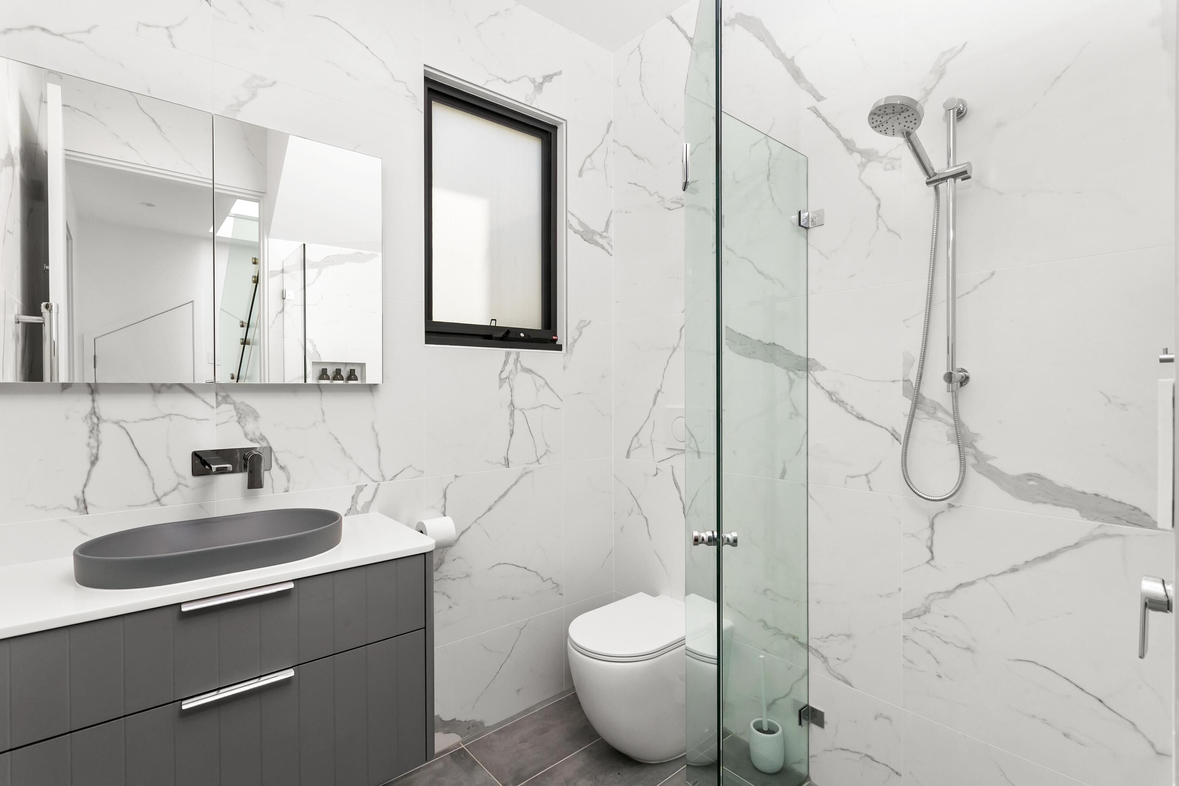 A modern bathroom with a marble sink, a glass shower enclosure, and a toilet.