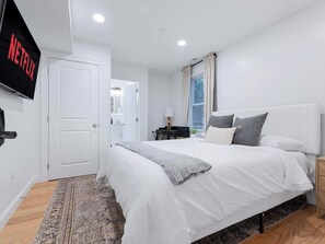 Une chambre à coucher avec un lit, une télévision, une porte et une fenêtre avec des rideaux.