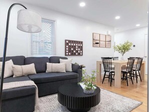 Una sala de estar moderna con sofá, mesa de centro, comedor, sillas y una lámpara.