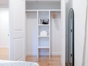 Un dressing avec des étagères blanches, une tringle à vêtements et une porte dotée d’une poignée noire.