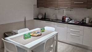 A modern kitchen with white cabinets, a dining table with chairs, and a small countertop with various appliances and items. - Bed&Bike (Aulla)